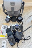 Main group shot showing camera body with lens, flash unit, camera bag, additional lens, manuals, leather cases