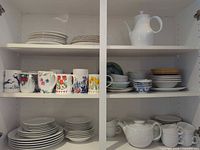 Cupboard view showing assorted white plates, mugs, bowls, teapot and pitcher