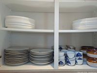 Cabinet shelves showing stacks of white plates, blue fish motif plates, matching cups and brown-amber soup bowls