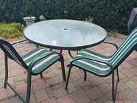 Round glass patio table with two matching sling chairs on patio surface
