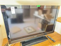 Front view of Sharp Aquos TV on stand with remote visible