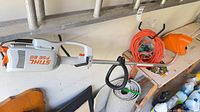 Trimmer mounted on wall with extension cord and guard visible