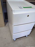 Front view of white 3-drawer rolling pedestal file cabinet showing lock and casters