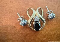 Pendant and pair of stud earrings laid out showing gemstones, gold settings, and earring backs