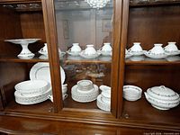 China cabinet shelf showing dinnerware set components: compote, cups, plates, serving bowls, covered tureen