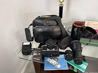 Group shot of camera body, lenses, flash, bag, cases, manuals and strap on glass table