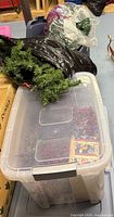 Clear tote with red berry stems next to blue tote holding green garland