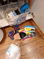 Lot showing two Finish rinse aid bottles, Glad trash bags box, scrub brush, plastic tote with cloths and gloves