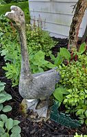 Front view of concrete goose statue in garden bed with metal sign at base