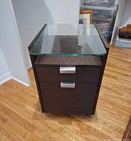 Front view of dark espresso cabinet with glass top and two silver-pull drawers on casters