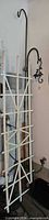 White trellis leaning against wall with black shepherd hook visible behind