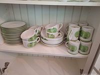 Shelved dinnerware showing plates, bowls, mugs, teacups with green apple motif