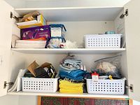 Overview of cabinet shelves with towels, baskets, mop pads, hardware items