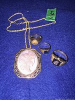 Necklace with cameo pendant and three 10K gold rings on blue background