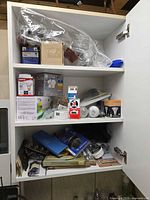 Full cabinet view showing mixed boxed bulbs, batteries, oil can, hardware