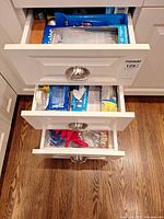 Open kitchen drawers showing boxed Ziploc bags, Reynolds wrap, Glad product, gloves and tape
