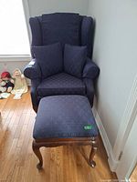 Front view of navy wingback chair with ottoman and pillows