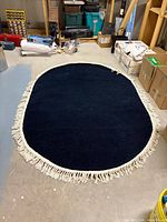 Full view of oval navy rug with white fringe