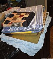 Stack showing light blue scalloped quilted placemats, rigid green cork-back placemats, blue-white stripe quilted cotton and patchwork quilted cotton
