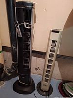Seville Classics black tower fan and Hampton Bay beige tower fan standing side by side showing full height and cords