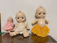 Front view of three vintage composition Kewpie-style dolls with clothing visible