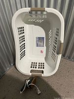Top view of white plastic laundry basket, tan handles, steamer visible with cord