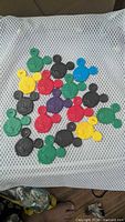 Group of 23 assorted colour Mickey Mouse balloon weights laid out on mesh surface