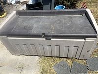 Front top view of grey Rubbermaid deck box showing black lid and surface wear
