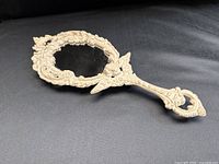 Angled view of painted cast iron hand mirror showing ornate frame and handle