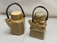 Two tan glazed Japanese ceramic teapots with rattan handles and lids on
