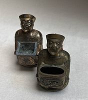 Front view of both brass figural incense burners showing openings and facial detail