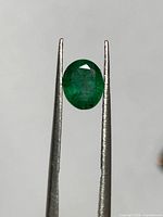 Front view of oval emerald held by tweezers
