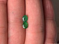 Two oval emeralds placed on fingertip showing size and faceting