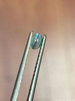 Gemstone held in tweezers, side profile showing translucency and cat’s eye band