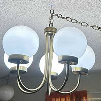 Full view of chandelier showing five white frosted glass globes, curved brass-tone arms and central column