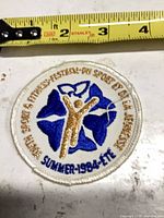 overall view of round embroidered patch showing colors, text and ruler for scale
