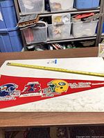 Front of red felt pennant showing Toronto Argonauts logo, 75th Grey Cup emblem, Edmonton Eskimos helmet and BC Place Stadium text with tape measure indicating length