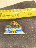 Front view of Daytona Speedweeks 1994 enamel lapel pin beside tape measure showing size