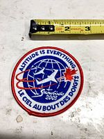 Front of round blue white red embroidered patch with globe, jet, maple leaf and text