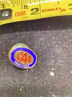 Front of oval CAA enamel pin beside tape showing ~5/8 in (16 mm) size