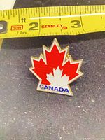 Front view of enamel maple leaf pin next to tape measure
