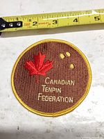 Front of round embroidered Canadian Tenpin Federation patch with measuring tape for scale