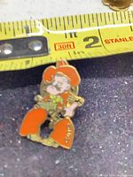 Front view of enamel cowboy cartoon lapel pin alongside tape measure showing height under 1 inch