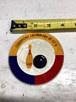 Front of round bowling federation patch beside tape measure showing approx 3.5 in