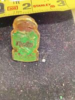 Front view showing green enamel shield design and tape for scale