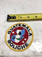 Front view of circular Guatemala BOLICHE patch beside ruler showing size