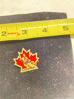Front view of enamel maple leaf pin with measuring tape showing size