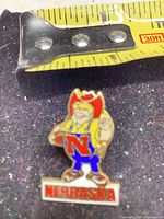 Front of enamel lapel pin showing mascot, colors, tape for scale