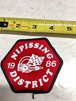 Front of red Nipissing District 1986 patch with tape measure for scale