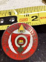 Front view of round OSU enamel pin next to tape measure